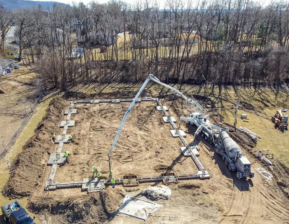 Aerial view of a boom pump pouring a house foundation, with a mixer truck at the hopper