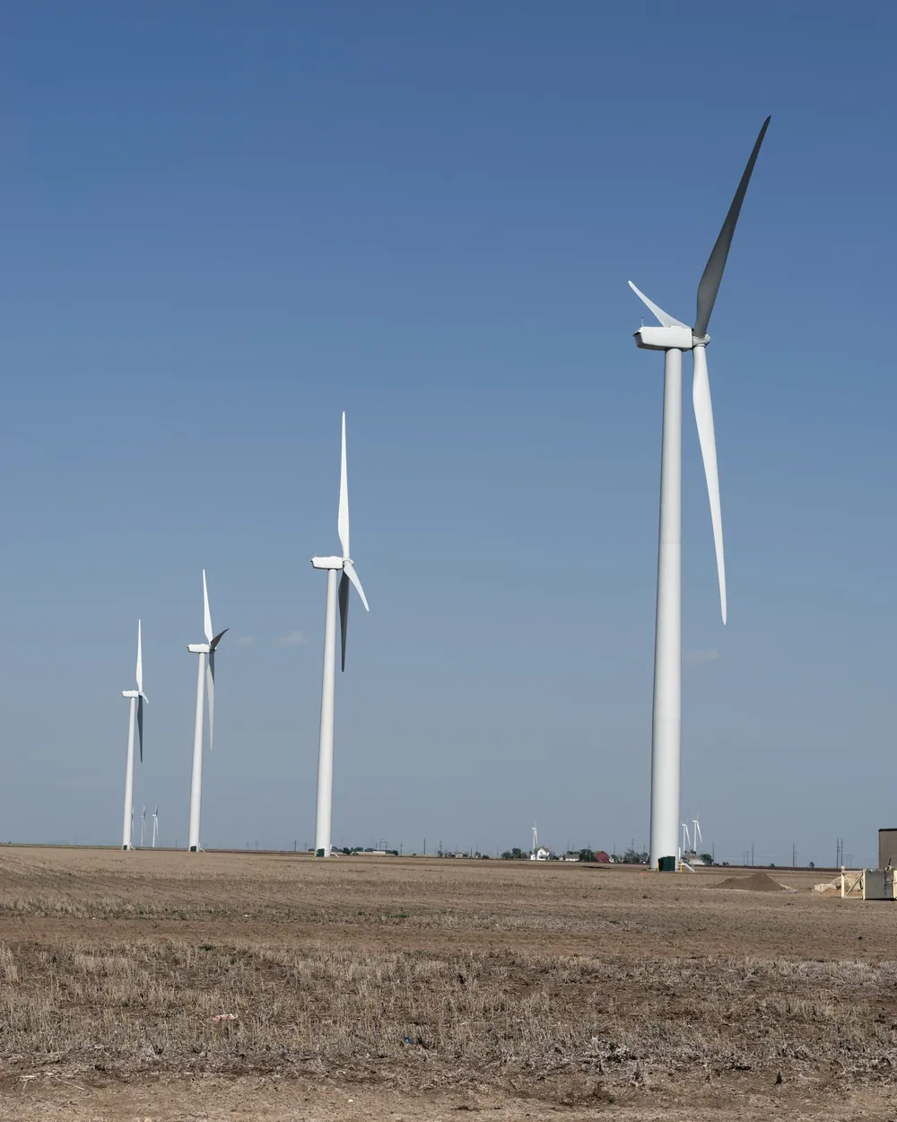 Wind turbines standing on flat farmland under a clear sky in rural Carson County, Texas